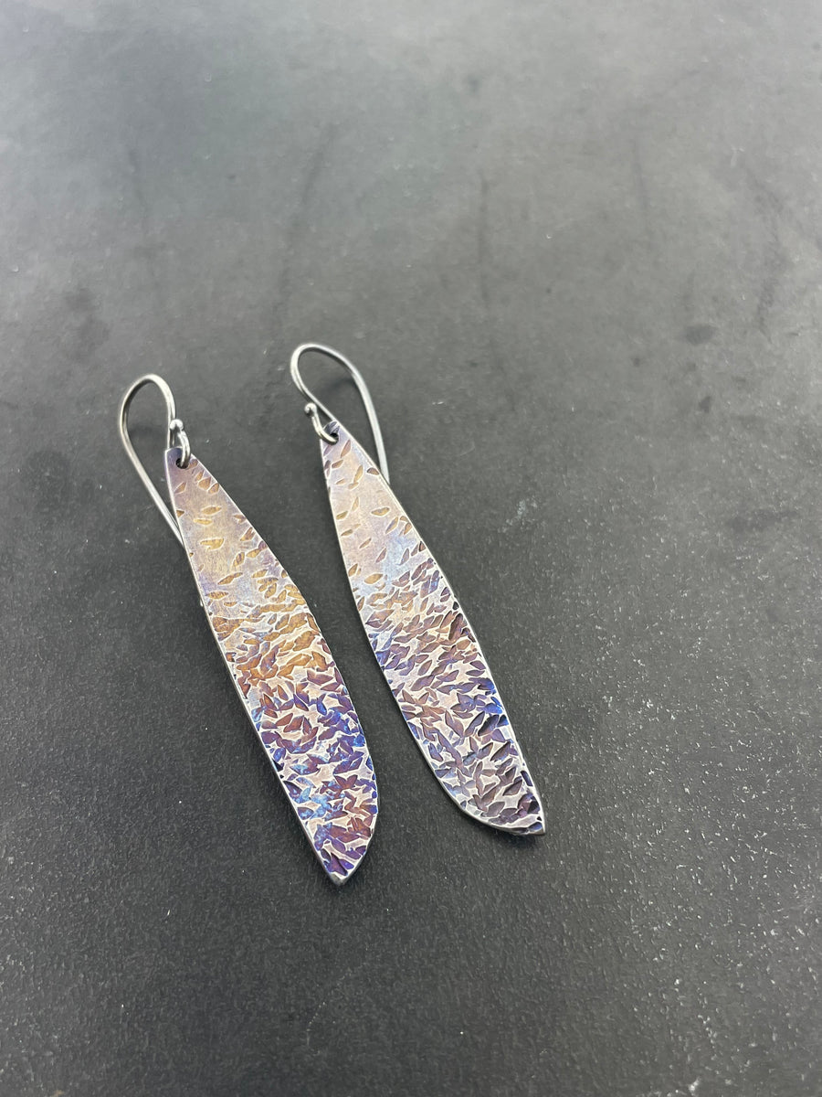 Pair of long, thin earrings with textured surface on a dark gray background